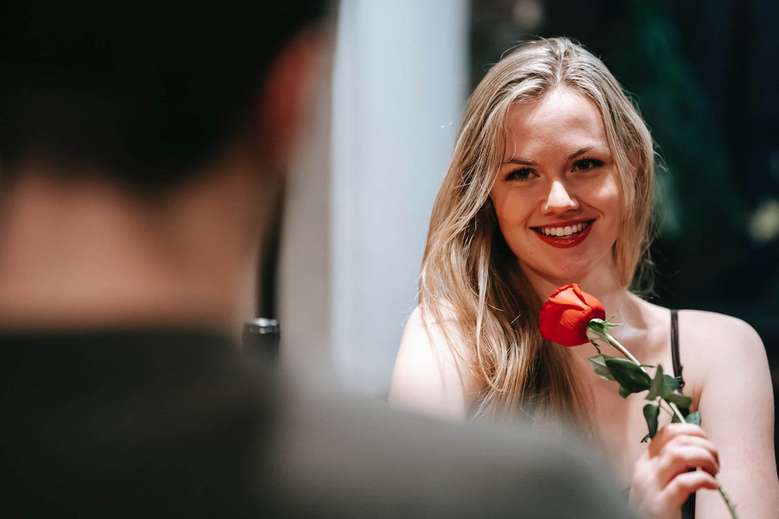 Une jolie jeune femme blonde en train de sourire et qui porte une rose rouge dans sa main | Watsunder